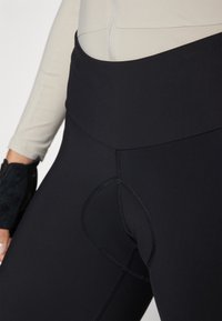 Zwarte high-waisted legging van soepel, stretchy materiaal. Beschikt over platte naden en een ronde uitsnijding aan de achterkant.