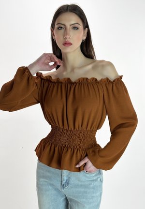 Rostfarbene, schulterfreie Bluse mit gerafftem Ausschnitt, geraffter Taille und langen Ärmeln. Weiche Textur und entspannte Passform. Kombiniert mit hellblauen Jeans.