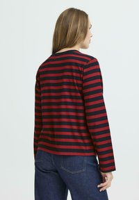 Red and navy striped long-sleeve shirt with a rounded neckline and a relaxed fit, made from soft, textured fabric.