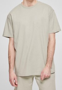 Beige bavlněné tričko s kulatým výstřihem, krátkými rukávy a volným střihem. Hladká textura, minimální přízi, jednoduchý design.