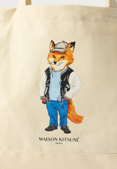 Tote de lona beige con un personaje de zorro ilustrado que lleva una gorra de béisbol, chaqueta varsity negra, camiseta azul y jeans azules.