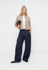 Beige strikkegenser med knapper, hvit skjorte, marineblå vide bukser med striper, svart clutch-veske og svarte leppestift. En enkel, uformell antrekk.