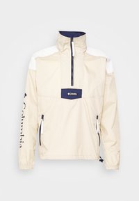 Ljusbeige pullover-jacka med dragkedja i halsen, marinblå och vita accenter, elastiska ärmslut och framsidan med logotyp. Har sidofickor med dragkedja.