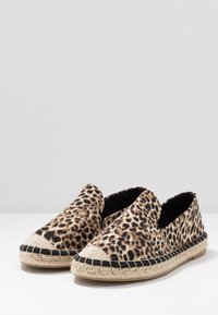 Espadrilles à imprimé léopard avec une semelle en jute tressé, un bord cousu noir et une tige en tissu lisse. Design sans lacets avec un bout arrondi.