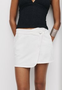 Witte denim mini rok met een wikkeldesign, voorzien van een voorste knoopsluiting en zijzakken. Gladde textuur met een nette afwerking.