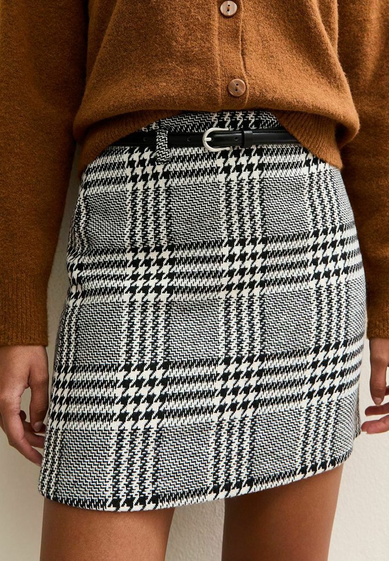 Mini falda de cuadros en blanco y negro con una tela texturizada, que presenta una cintura alta y un cinturón negro con una hebilla de plata.