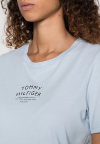 Camiseta de algodón azul claro con cuello redondo y mangas cortas. En la parte frontal muestra un texto de logo negro con detalles de establecimiento.
