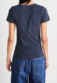 Námorně modré bavlněné tričko s krátkými rukávy a kulatým výstřihem, spárované s vysokými volnějšími džíny s viditelnými kapsami.