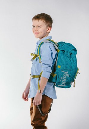 Zaino turchese con un motivo testurizzato, spallacci regolabili gialli e un logo frontale. Indossato da un bambino con una maglietta azzurro chiaro e pantaloni marroni.