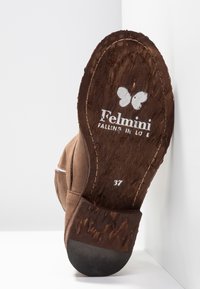 Semelle d'une chaussure marron avec un logo papillon, nom de la marque "Felmini", phrase "Falling in Love" et taille 37 visible.