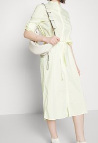 Abito midi a strisce giallo chiaro con colletto, vita con cinturino e maniche corte; abbinato a una borsa a tracolla crema.