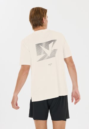 Man wearing cream-colored T-shirt with black geometric design on the back and black shorts, standing facing away on a white background.