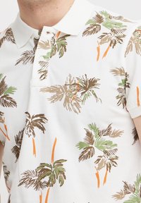 Witte polo-shirt met een palmbomenpatroon in groen, bruin en oranje. Het heeft een klassieke kraag en een knopenlijst. Struikgewas stof.