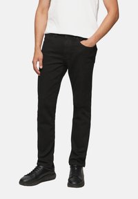 Pantalones de mezclilla negros con corte ajustado, que cuentan con cinco bolsillos, trabillas para el cinturón y una textura suave, combinados con zapatos negros.