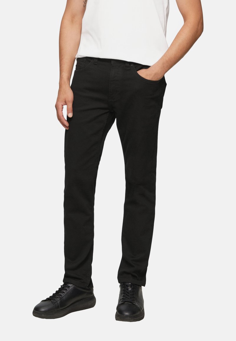 Pantalones de mezclilla negros con corte ajustado, que cuentan con cinco bolsillos, trabillas para el cinturón y una textura suave, combinados con zapatos negros.