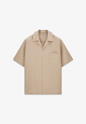 Chemise beige à manches courtes avec boutons, col camp et poche poitrine, posée à plat sur fond blanc.