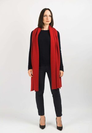 Écharpe rouge en tissu doux, portée sur un pull noir, associée à un pantalon slim noir et des escarpins. Design simple, sans motifs.
