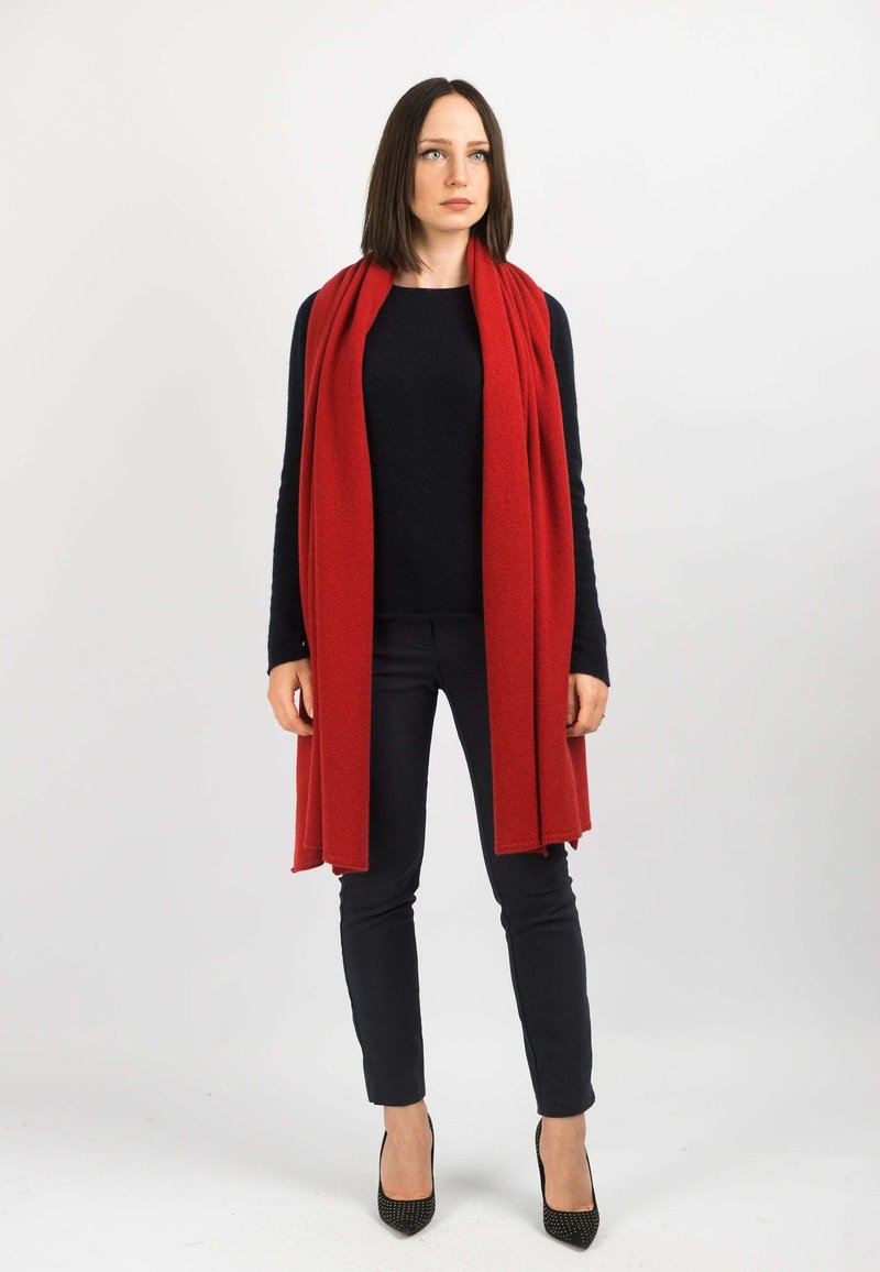 Rød tørklæde lavet af blødt stof, båret over en sort sweater, parret med sorte slim pants og højhælede sko. Enkel design, uden mønstre.