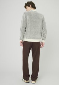 Cardigan tricoté gris et blanc avec un col crème, associé à un pantalon marron. Coupe amples, poignets et ourlets côtelés. Chaussures décontractées.