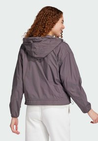 Lätt, kort jacka i dämpad grått tyg med huva. Har elastiska ärmslut, justerbar nederkant och en slät textur.