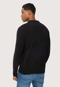 Schwarzer gestrickter Pullover mit strukturiertem Finish, rundem Halsausschnitt und geripptem Saum sowie Bündchen, kombiniert mit blauen Jeans.