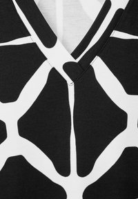 Svart T-shirt med ett djärvt vitt abstrakt mönster. V-ringning med kontrasterande texturer mellan tyget och mönsterdetaljerna.