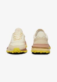 Zapatillas en beige y crema con materiales de ante y malla, que presentan suelas texturizadas, acentos amarillos y un diseño en capas y curvado.