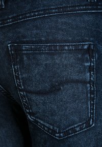 Dark blue denim back pocket with subtle decorative stitching on a pair of jeans.