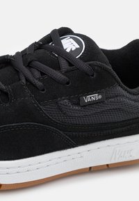 Black sneaker made of suede and mesh, featuring black laces, a white sole, and a small Vans logo tag on the side.