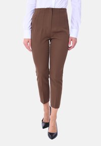 Pantaloni marroni a vita alta con pieghe, dotati di tasche laterali e un design sagomato, abbinati a décolleté nere a punta.