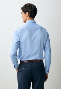 Camicia da uomo azzurro chiaro con texture, maniche lunghe e polsini dettagliati, abbinata a pantaloni scuri e cintura marrone.