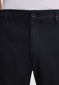 Pantaloni neri con texture, dotati di chiusura a bottone in vita e una finitura liscia, con un motivo sottile che attraversa il tessuto.