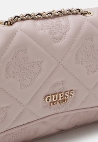 Sac à main matelassé rose clair avec logos embossés, bandoulière chaîne dorée, et marquage métallique doré "GUESS EST 1981" à l'avant.