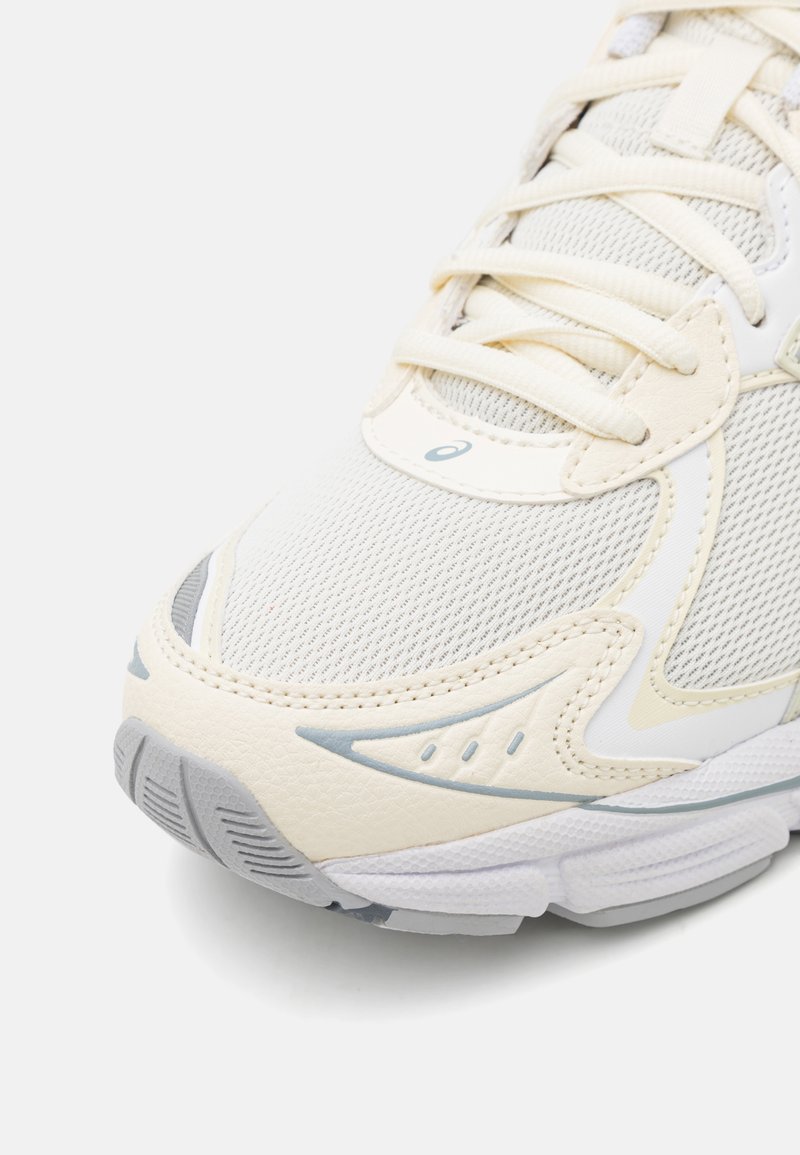 Sportlicher Schuh mit einem Obermaterial aus Netzgewebe in Creme und Hellgrau, ausgestattet mit strukturierten Akzenten, schmalen Schnürsenkeln und einer robusten Gummisohle mit Rillen.