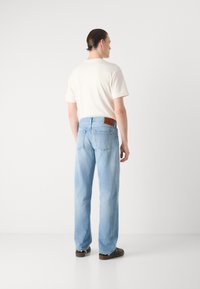 Ljusblå denimjeans med avslappnad passform, med en brun läderpatch vid midjan och fransat avslut. Bärs med en krämfärgad t-shirt.