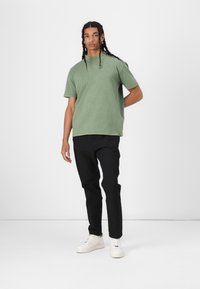 Grön bomulls t-shirt med avslappnad passform, korta ärmar och rund halsringning, matchad med svarta byxor och vita sneakers.