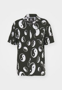 Chemise noire à manches courtes avec des motifs yin-yang blancs, fermeture à boutons à l'avant et une poche poitrine. Fabriquée en tissu doux.