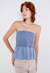 Blå denim strapless topp med smocket liv, utsvingt peplumkant og mykt teksturert stoff. Enkel design uten mønstre.