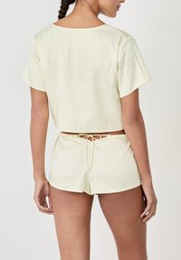 Lichtgele lounge-outfit met een cropped top met korte mouwen en bijpassende shorts, beiden met een subtiel, textuurpatroon. Verstelbare tailleband.
