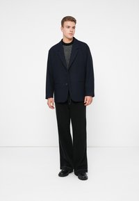 Námornícky oversized blazer s jedným gombíkom, v kombinácii s čiernym pleteným topom a širokými čiernymi nohavicami. Hladké textúry a minimalistický dizajn.