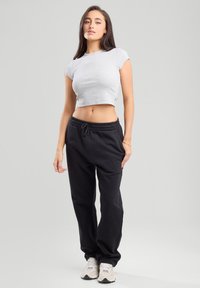 Harmaa lyhythihainen t-paita, joka on yhdistetty mustiin collegehousuihin, joissa on kiristysnauha vyötäröllä ja sivutaskut. Mallilla on jalassaan vaaleat urheilukengät.