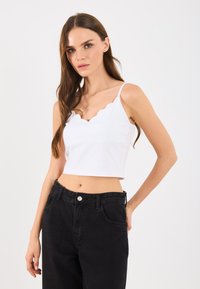 Witte cropped tanktop met geschulpte halslijn en dunne bandjes, gecombineerd met hoge, zwarte spijkerbroek. Soepele katoenstructuur.