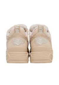 Baskets beiges avec une doublure en peluche, une forme arrondie et des semelles texturées. Présentent un logo argenté et une languette en tissu avec lettrage.