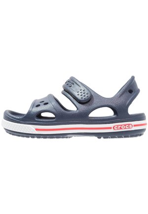Sandales Crocs bleu marine avec deux sangles réglables, trous de ventilation, et semelle blanche avec des accents rouges et blancs. Matériau en caoutchouc texturé.