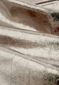 Metallischer Stoff mit einer rissigen Textur, in glänzendem Silber und glatter Oberfläche, gefaltet, um seine reflektierenden Eigenschaften zu zeigen.