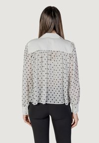 Blusa bianca a pois con retro trasparente, dettagli arricciati e colletto bianco solido. Maniche lunghe con polsini abbottonati.