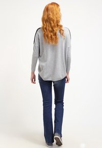 Pull gris oversize avec des accents noirs sur les côtés, associé à un jean évasé bleu foncé et des baskets grises, présentant une texture douce et une coupe décontractée.