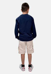 Maglietta a maniche lunghe navy, pantaloni cargo beige e sneaker bianche con dettagli rossi, viste da dietro. Design semplice, dettagli minimali.