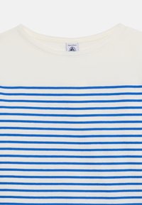 Λευκό μπλουζάκι με στρογγυλή λαιμόκοψη και στενές οριζόντιες μπλε ρίγες, με ορατή ετικέτα που αναγράφει μέγεθος 8 ετών/128 εκ. μέσα στο γιακά.