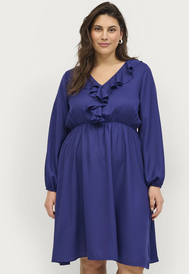 Vestido morado con escote en V, mangas largas y detalles con volantes a lo largo del busto. Tela suave y fluida con una cintura elástica.